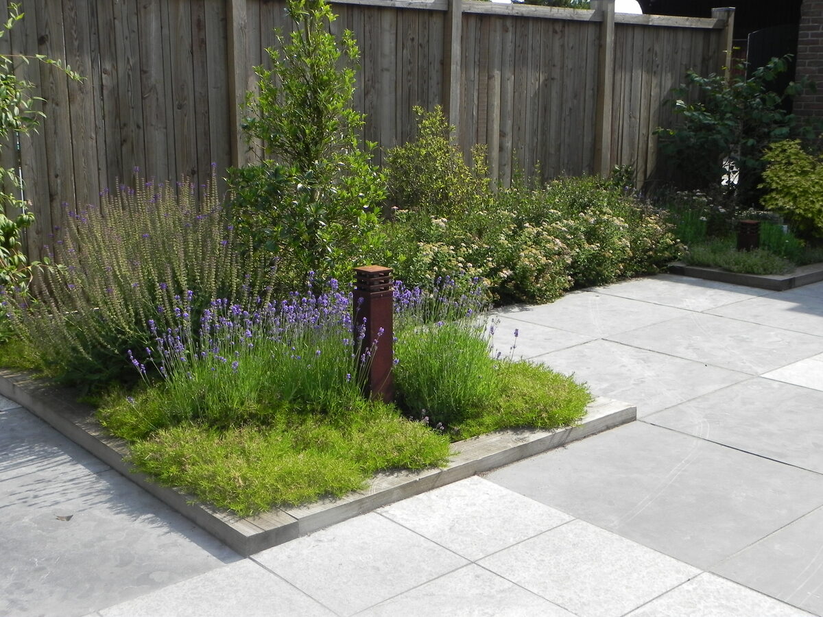 Moderne tuin met grijze terrastegels, lavendelborder en cortenstalen tuinlamp